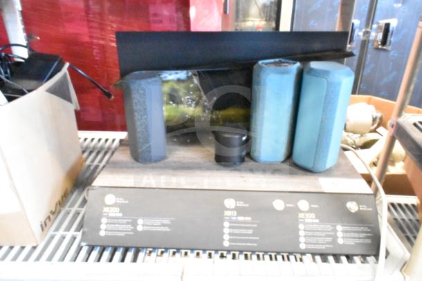 Speaker store display featuring three portable Bluetooth speakers in various colors. Display shows model information.