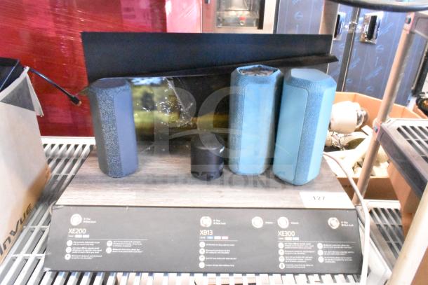 Speaker store display featuring 3 portable Bluetooth speakers: XE200, XB13, XE300 models. Includes product information.