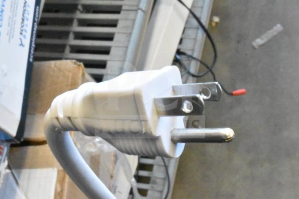 A close-up of a white electrical plug on a coiled cable, against a background of assorted boxes and wires.