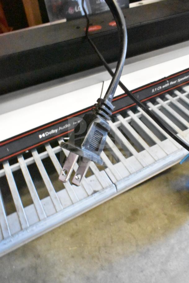 LG store display featuring a sound bar and speaker. Includes power plug and Dolby Audio marking, indicating surround sound capability.