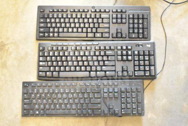 Three black computer keyboards on a concrete floor; includes HP and Logitech models. Good condition with visible key labels.