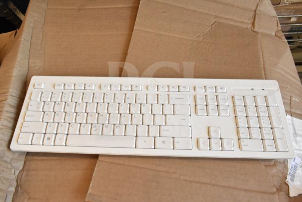 White HP computer keyboard in good condition, on a cardboard surface. Part of a 40-item lot including keyboards and mice.