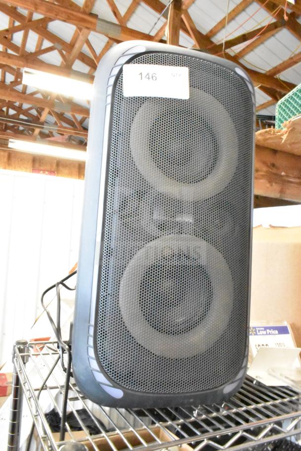 Large black speaker with dual drivers, metal grille, and visible label "146." Good condition, resting on a wire shelf.