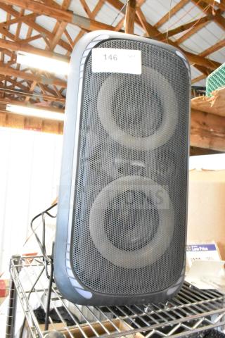 Large black speaker with dual drivers, metal grille, and visible label "146." Good condition, resting on a wire shelf.