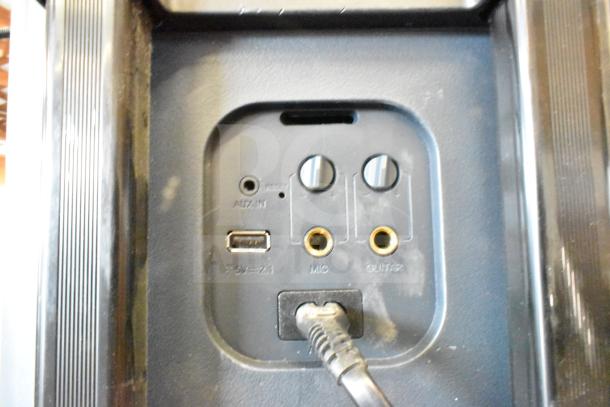 Speaker connection panel with AUX, USB, MIC, and GUITAR inputs. Features metal knobs and connected power cable.