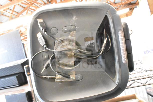 Black speaker with USB and audio cables, featuring control buttons on top, including power and Bluetooth. Modern design in good condition.