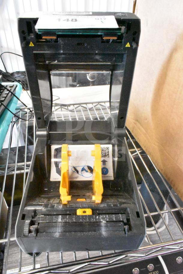 Zebra ZD620 Thermal Barcode Printer, open lid, visible yellow guides, QR code label, commercial shelving.