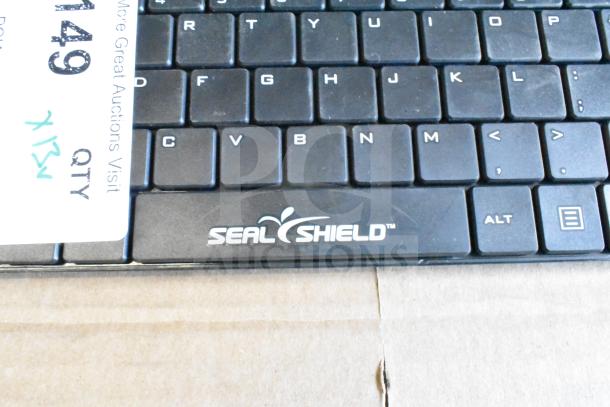 13 Seal Shield keyboards, black with white lettering, used condition, visible branding, lot of 13 for auction.
