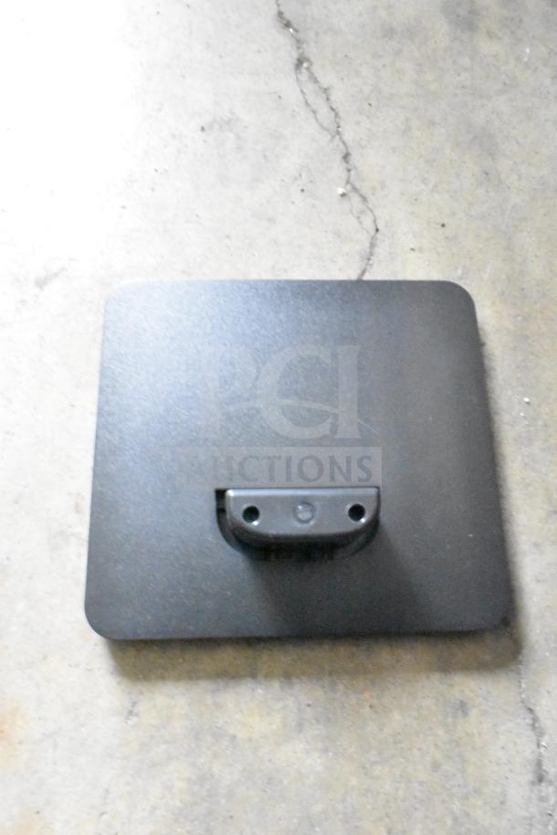 Black rectangular mounting bracket on concrete floor, part of a mixed lot of various items including cables.