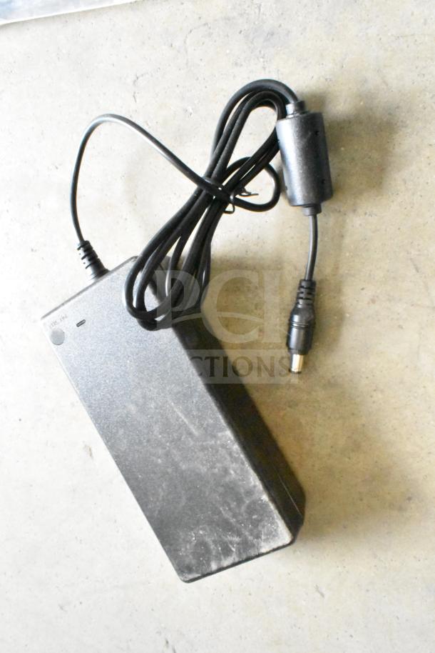 Black power adapter with attached cable, featuring a cylindrical connector. Appears used with visible wear.