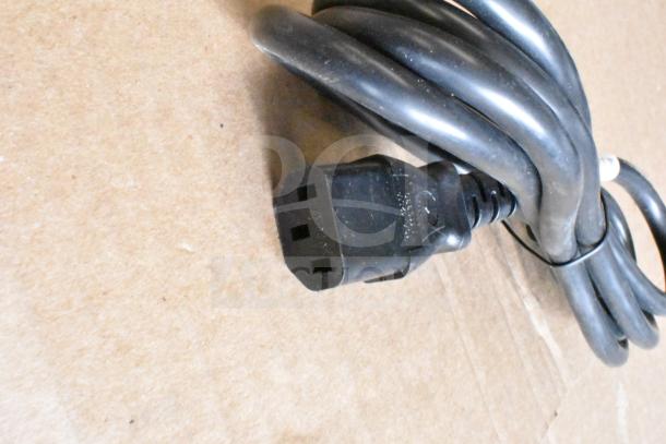 Coiled black power cable on cardboard surface, showing three-prong connector; part of mixed item auction lot.