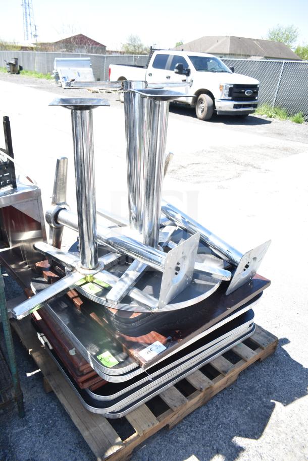 Stacks of assorted tabletops and table bases, metal bases with mounting plates on wooden pallets. Includes 17 pieces.