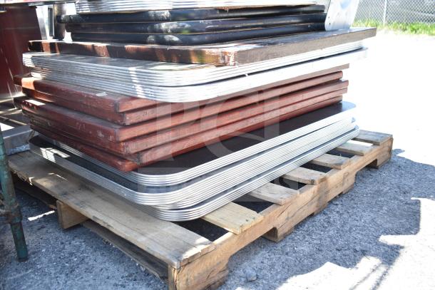 Stack of assorted tabletops and table bases on a wooden pallet, showing various metal and wood finishes.