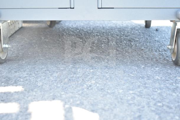 Gray metal unit with 3 compartments on commercial casters, in good condition, suitable for storage and mobility.