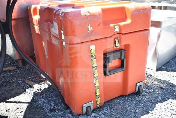 Large orange storage case with a handle, wheels, and caution tape. Shows signs of wear and includes metal clasps for security.