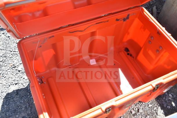Orange plastic case with open lid, showing interior wear and small stains. Visible screws and markings add detail. Rugged build.
