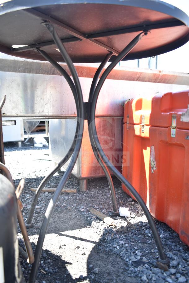 Steel round table with curved legs, industrial style. Some wear visible, suitable for outdoor use. Two available in auction.