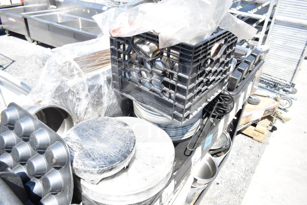 Black poly 2-tier cart filled with cookware including skillets and poly bins, some items wrapped in plastic, in fair condition.