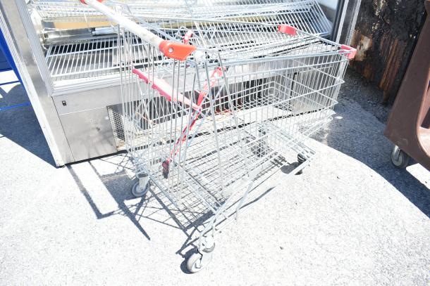 Metal shopping cart on casters with red handles, light wear. Ideal for retail use, sturdy and easy to maneuver.