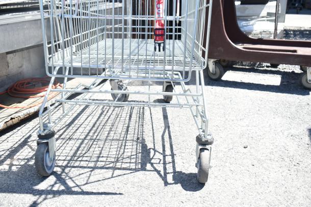 Shopping cart with metal frame and four swivel casters, in used condition, ideal for retail use.