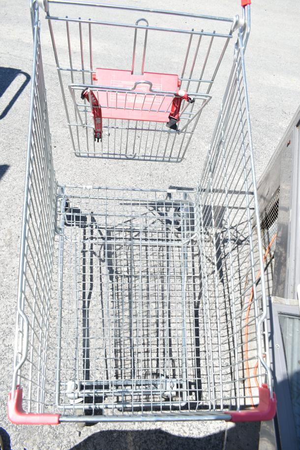 Metal shopping cart with red handles and child seat, on casters, showing good condition, outdoor setting.