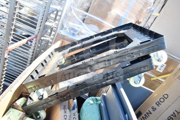 Stacked items including plastic carts with casters, visible cardboard boxes, brand new and marked for auction.