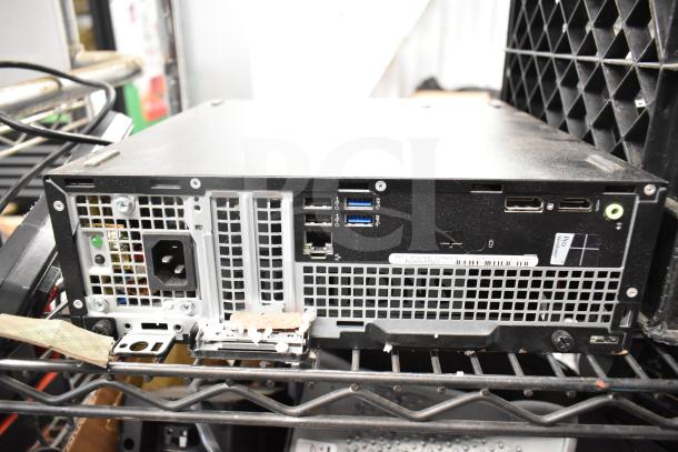 Dell computer tower with multiple USB ports, audio jacks, and power supply connection. Moderate wear, some markings.
