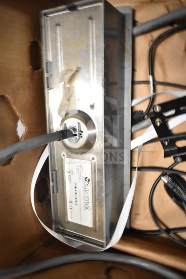 A lot of mixed items, including Sensormatic ZBSTPSP-L device and various cables in a brown box, showing tags and connectors.