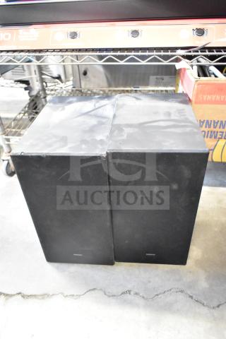 Two Samsung PS-WB65D wireless subwoofers, black, in good condition, placed on a metal shelf.