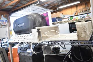 "Rave+ store display with electronic unit, black speaker, industrial setting, metal shelves, wires visible."