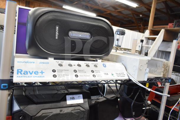 Soundcore Rave+ Partycast speaker on display with features listed. Includes two additional electronic units, condition visible.