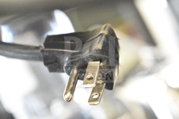 Close-up of a black three-pronged power plug; part of an auction lot including store display and electronics.