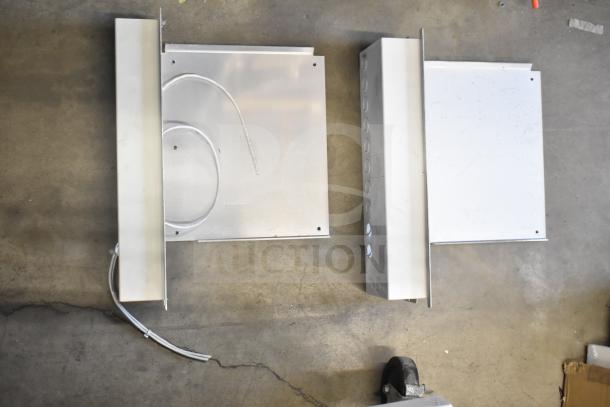 Three metal electronic enclosures, each with wiring and rectangular shapes, displayed on a concrete surface; condition varies.