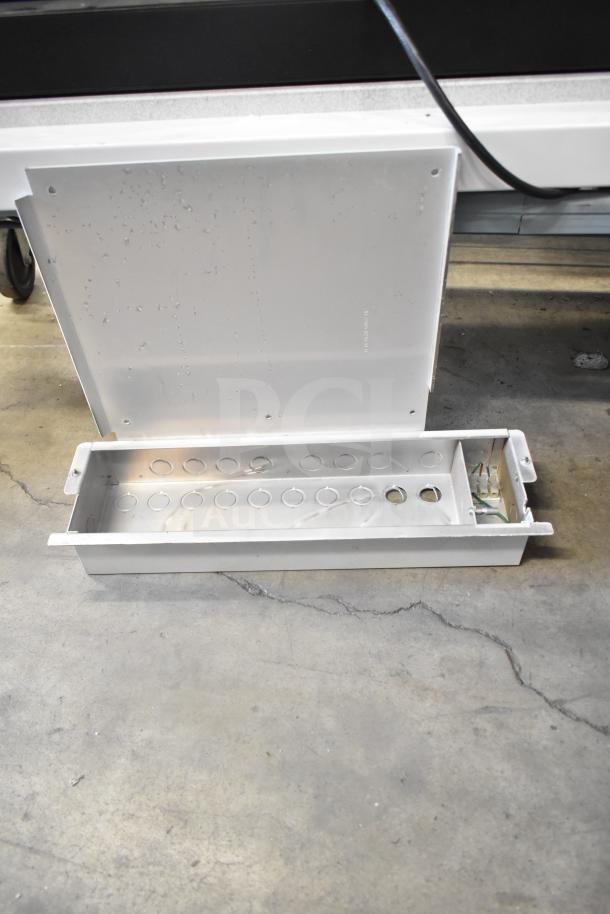 Metal electrical enclosure box with lid open, showing multiple circular cutouts and wiring. Appears slightly worn.