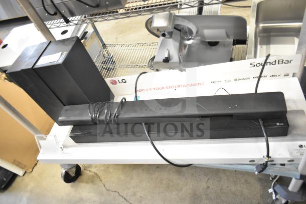 LG store display with sound bar and two speakers. Includes visible cords and labels. Ideal for enhancing audio setups.