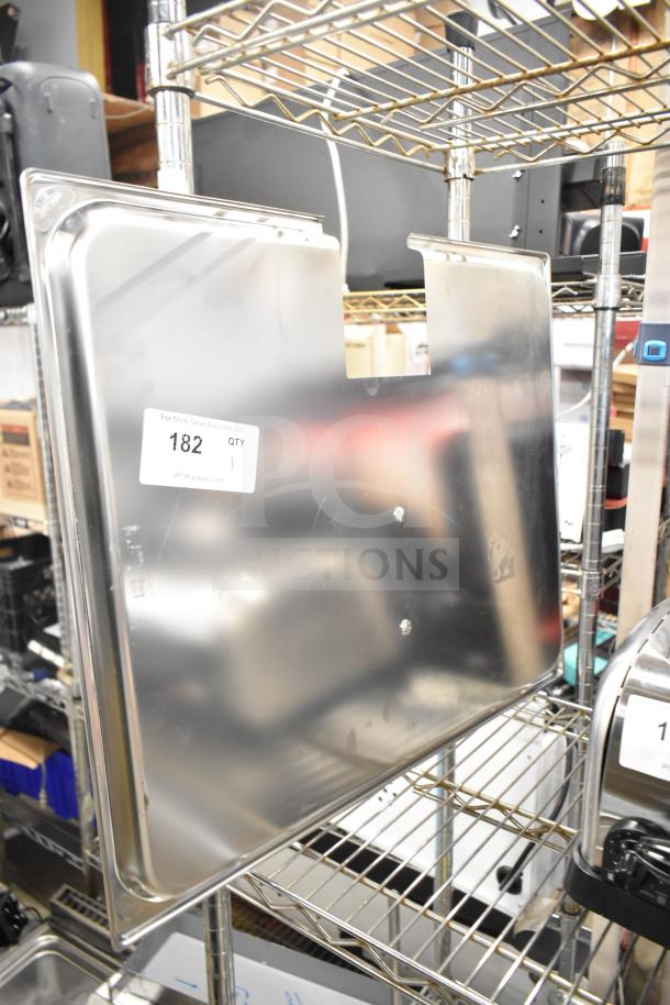 Brand new metal lid with minor scratches and dents, shown on metal shelving. Features auction tag labeled "182 QTY 1."