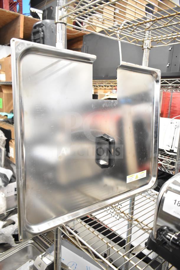 Brand new metal lid with handle, minor scratches, reflective surface, rectangular shape. Industrial storage setting.