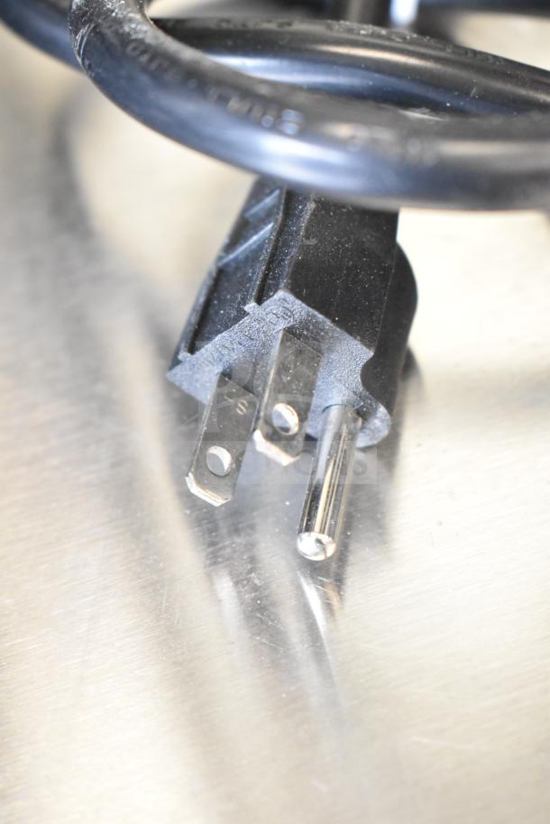 Close-up of a three-prong electrical plug attached to a black cord, part of the Avantco 177HDC26 heated display case.