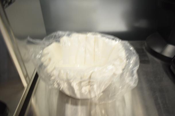 Blurred image of a wrapped item, possibly related to coffee brewing equipment, on a reflective surface.