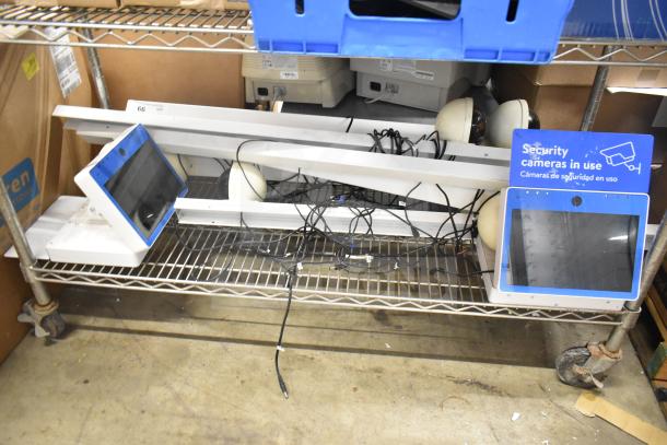 Security system setup with 2 monitors and cameras on a metal shelf. Cables visible, "Security cameras in use" sign shown.