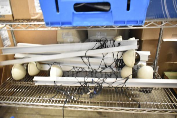 Security system setup with two monitors, several cameras, wires, and mounting hardware on a metal shelf. Some items appear used.