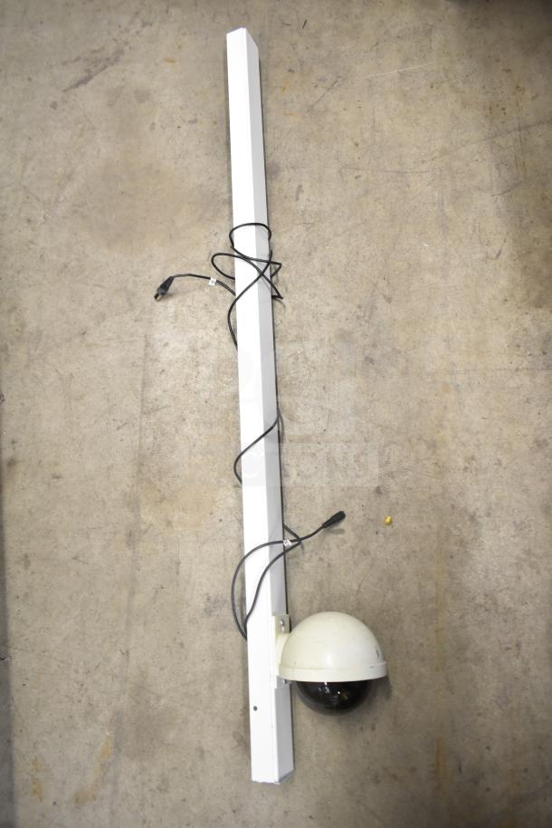 Security camera on a white mounting beam with attached power cables, part of a security system setup; camera in used condition.