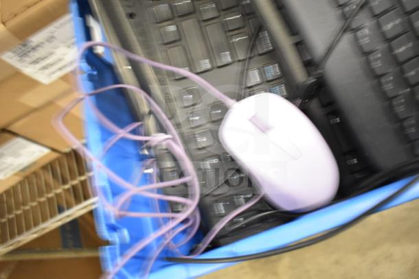 Blurred image of various computer items in a bin, including keyboards and a white mouse, tangled wires visible.