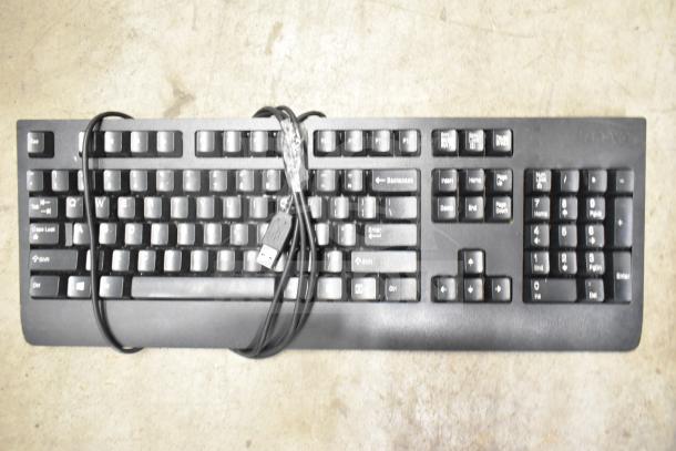 Black Lenovo wired computer keyboard with USB connector on concrete surface.