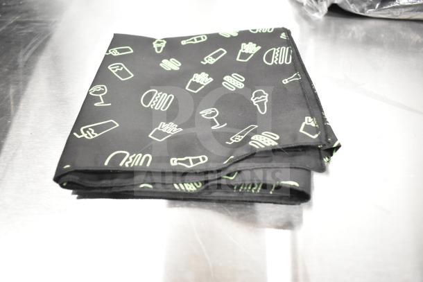 7 new scratch and dent Shack Staff Tees with various sizes on a metal table. Features playful food icon print.