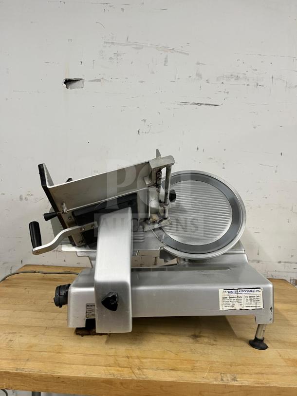 Steel manual food slicer on wooden table, features adjustable blade, robust design, and used condition.