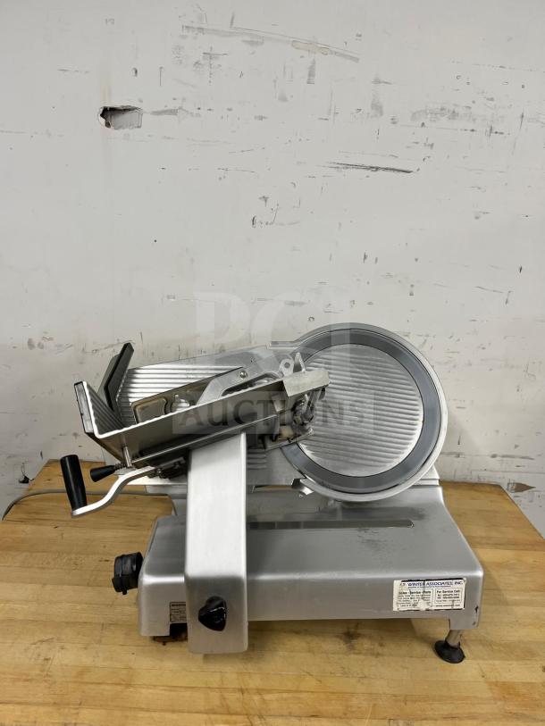 Steel manual food slicer in good condition on wooden surface, features sharp blade, adjustable thickness, and grip handle.