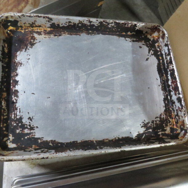 Approximately 30 used half-size sheet pans with visible wear, including scratches and burnt edges.