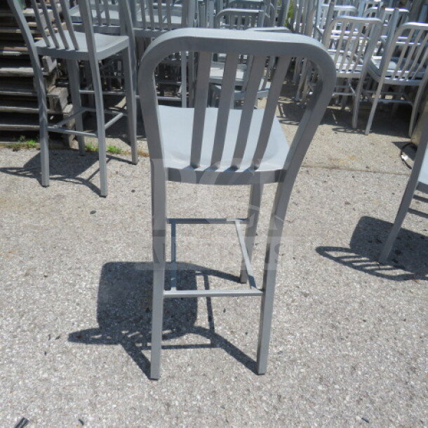 Silver metal bar height chair, slatted back, pristine condition, stackable design, durable for indoor/outdoor use.