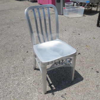 Silver aluminum indoor/outdoor chair with slatted back, sturdy design. Slight surface wear, suitable for versatile use.